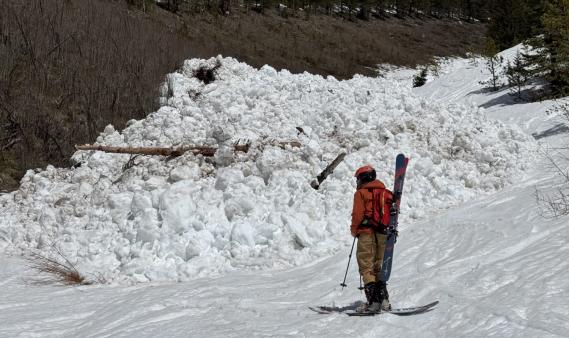 Person standing near a pile of avalanche debris on a sunny day. 